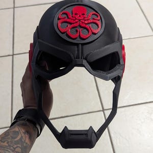 May include: A black 3D printed helmet with a red and black Hydra logo on the front. The helmet has a visor and a chin strap.