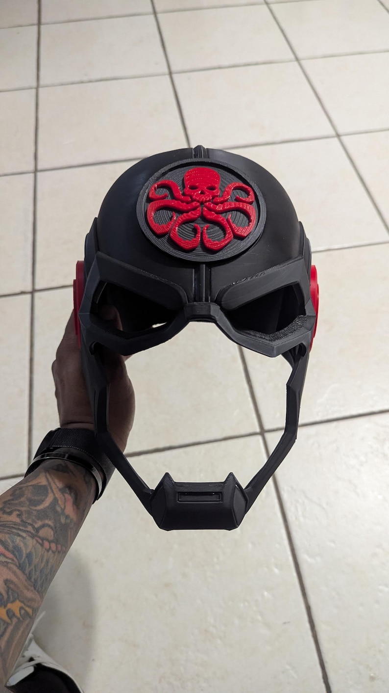 May include: A black 3D printed helmet with a red and black Hydra logo on the front. The helmet has a visor and a chin strap.