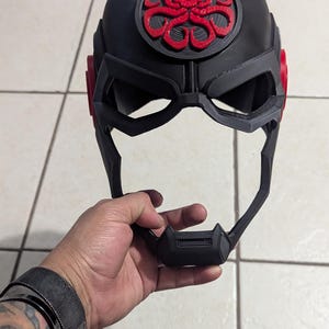 May include: A black and red 3D printed helmet with a skull and tentacles design. The helmet has a visor and a chin guard.