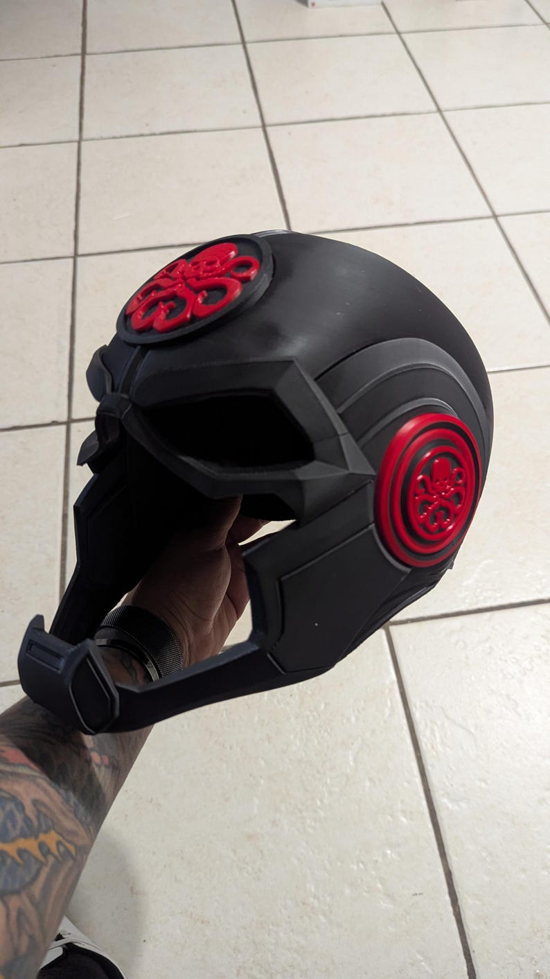 May include: A black helmet with a red Hydra logo on the front and side. The helmet has a futuristic design with a visor and a chin guard.