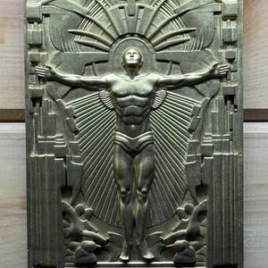 May include: A bronze-coloured relief sculpture depicting a muscular male figure with outstretched arms, set against a sunburst design. The artwork has an Art Deco style, with architectural elements framing the central figure.