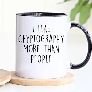 May include: White ceramic mug with a black rim and handle. The mug has black text that reads "I like cryptography more than people."