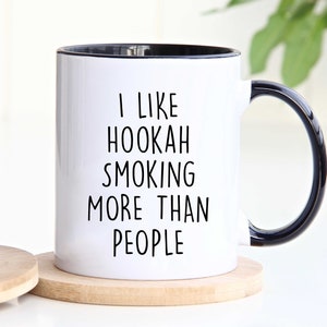 May include: White ceramic coffee mug with a black rim and handle. The mug has black text that reads "I like hookah smoking more than people".