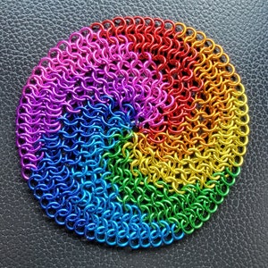 Op de afbeelding: Een regenboogkleurige kettingbaardcirkel, gemaakt van kleine metalen ringen, met een spiraalpatroon.