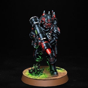 May include: A detailed miniature figure of a soldier in black armour with red highlights, carrying a large weapon. The figure is on a circular base with green crystals and a brown rim, against a dark backdrop.