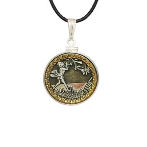 May include: A silver pendant necklace with a round, gold-rimmed charm featuring a detailed depiction of a fairy blowing on a flower. The fairy is silver, and the flower is gold. The background is a dark green and brown.