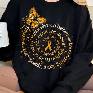 May include: Black sweatshirt with a gold butterfly and the text "Nothing about appendix cancer awareness but those who win battles we know more not those who show strength the strongest people are in front of us but those" in a circle around the butterfly.