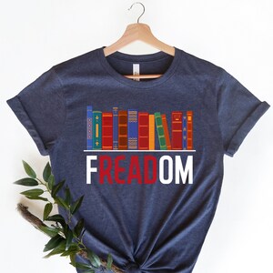May include: A navy blue t-shirt with a graphic of a bookshelf full of colorful books and the word "FREEDOM" in red and white letters.