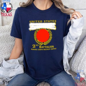May include: A navy blue short-sleeved t-shirt featuring yellow text and a graphic design. The print includes the words UNITED STATES, 2ND BATTALION, and MARINE CORPS RECRUIT DEPOT, surrounding a central yellow laurel wreath and a solid red circle.