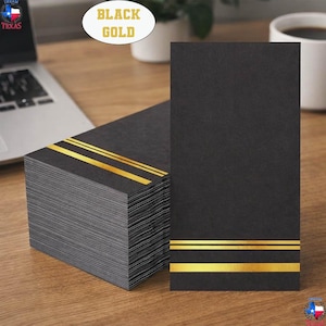 May include: A stack of rectangular black paper cards featuring two horizontal gold foil stripes near the bottom edge. The cards have a matte texture and a clean, sharp-edged design. The text BLACK GOLD is visible in a white oval above the stack.