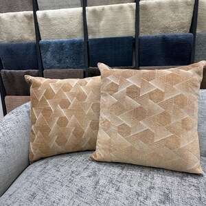 May include: Two beige throw pillows with a geometric pattern on a gray couch. The pillows are made of a soft, textured fabric.