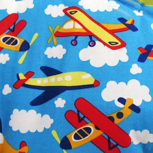 May include: A bright blue fabric featuring a repeating pattern of colorful airplanes and white clouds. The airplanes are depicted in various styles and orientations, colored in shades of red, yellow, and dark blue, scattered across the sky background.
