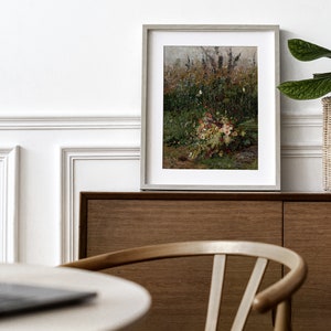 Pode incluir: Uma pintura emoldurada de um buqu&ecirc; de flores silvestres em um campo. A pintura est&aacute; em uma moldura cinza clara e est&aacute; pendurada em uma parede acima de um arm&aacute;rio de madeira.