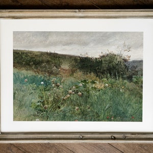 May include: A framed landscape print featuring a field of tall green grass and wildflowers under a cloudy sky. The artwork is in a silver-toned frame, adding a touch of elegance to the natural scene. The print evokes a sense of tranquility.