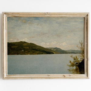 Puede incluir: Una pintura enmarcada que representa una escena de paisaje con un lago, montañas y árboles. El cielo es de color azul claro con nubes blancas. La pintura está en un marco de madera claro.