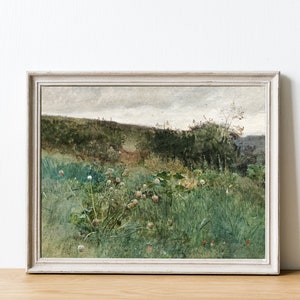 May include: A framed landscape painting featuring a field of tall green grass and wildflowers. The artwork has a muted color palette with shades of green, brown, and gray. The painting is in a white wooden frame, and the overall aesthetic is rustic and vintage.