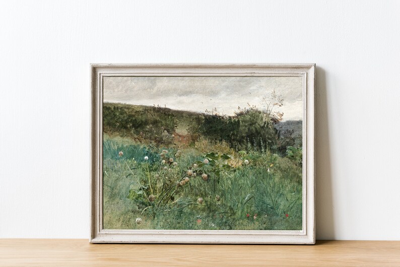 May include: A framed landscape painting featuring a field of tall green grass and wildflowers. The artwork has a muted color palette with shades of green, brown, and gray. The painting is in a white wooden frame, and the overall aesthetic is rustic and vintage.