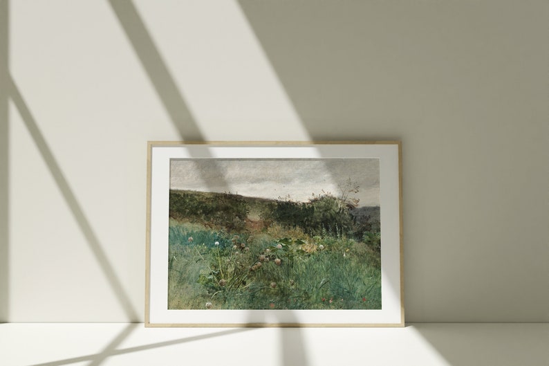 May include: A framed landscape art print featuring a field of green grass and wildflowers under a cloudy sky. The artwork has a vintage aesthetic with muted colors and a natural wood frame.