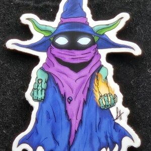 May include: A colorful sticker featuring a cartoon wizard with a blue hat and robe, a purple scarf, and green ears. The wizard holds a flame in one hand and has a black face with white eyes. The sticker has a white border.