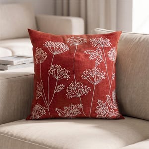 May include: A square scatter cushion in a deep rust-red colour featuring a white embroidered botanical pattern of cow parsley or similar umbellifer flowers with delicate stems and leaves across the front surface of the fabric cover.