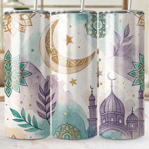 May include: A set of three stainless steel tumblers with a watercolor design. The design features a crescent moon, stars, mosque, and floral elements in shades of beige, teal, and purple. The tumblers have a silver lid and straw.