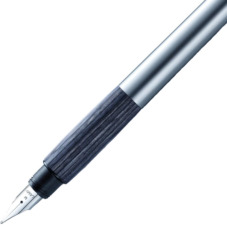 May include: A silver and grey fountain pen with a wood-grain pattern on the barrel. The pen has a metal nib with the word "LAMY" and the letter "M" engraved on it.