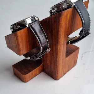 May include: Two watches with brown and black leather bands are displayed on a wooden watch stand. The stand is made of light brown wood and has a simple design.