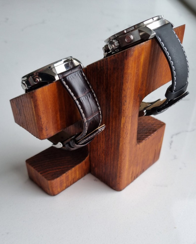 May include: Two watches with brown and black leather bands are displayed on a wooden watch stand. The stand is made of light brown wood and has a simple design.