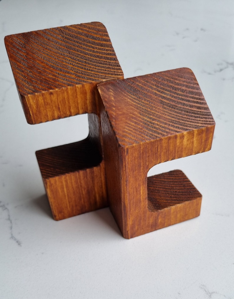 May include: A wooden sculpture made of two interlocking pieces, each with a unique shape and a smooth, brown finish.