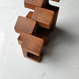 May include: A wooden sculpture made of five stacked blocks, each with a unique shape and a smooth, brown finish.
