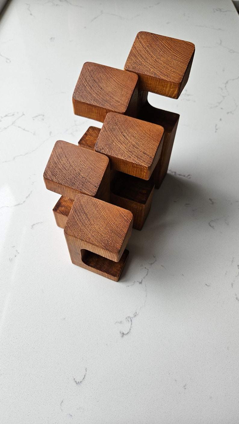 May include: A wooden sculpture made of five stacked blocks, each with a unique shape and a smooth, brown finish.