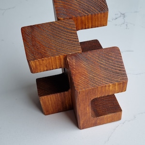 May include: A wooden sculpture made of four connected blocks. The blocks are stacked in a staggered pattern and have a rich brown color. The wood has a textured grain.