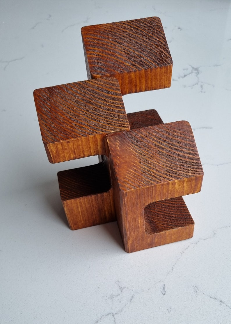 May include: A wooden sculpture made of four connected blocks. The blocks are stacked in a staggered pattern and have a rich brown color. The wood has a textured grain.