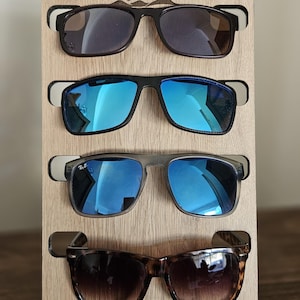 May include: Wooden sunglasses stand with four pairs of sunglasses. The stand features a sun and mountain design. The sunglasses are in various colours and styles.