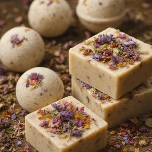 May include: A close-up of bath products, including four round bath bombs and three square soaps. The soaps and bath bombs are light beige and decorated with dried flowers in shades of purple, pink, and yellow. The products are arranged on a wooden surface.