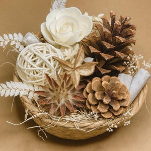 以下が含まれることがあります： 白い木製のバラ、松ぼっくり、星型の種子鞘、編みボールを特徴とする、織りバスケットの装飾的なアレンジメント。 このアレンジメントには乾燥した小枝が含まれており、ニュートラルな背景に設定されています。