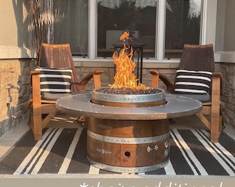 Könnte beinhalten: Ein Feuerschalen-Tisch aus einem wiederverwendeten Weinfass mit einer Metallplatte und einer Feuerstelle. Der Feuerschalen-Tisch ist umgeben von einem schwarz-weiß gestreiften Teppich und zwei Holzstühlen mit schwarz-weiß gestreiften Kissen. Der Text *Stühle zusätzlich* befindet sich am unteren Rand des Bildes.