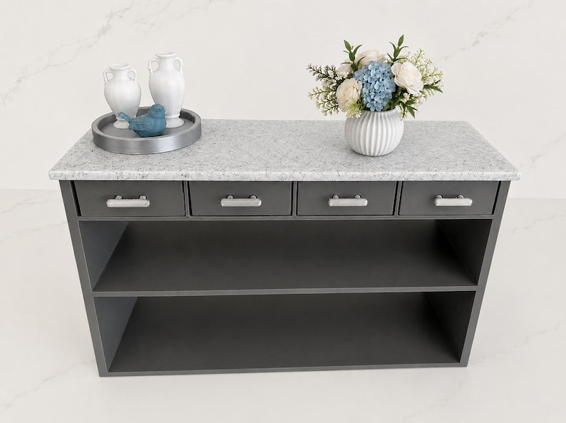 Pu&ograve; includere: Una console grigio scuro con un piano in pietra grigio chiaro maculato, quattro cassetti con maniglie argentate e due ripiani aperti. Sopra ci sono due vasi bianchi, una statuetta di uccellino blu su un vassoio grigio e un vaso con fiori.