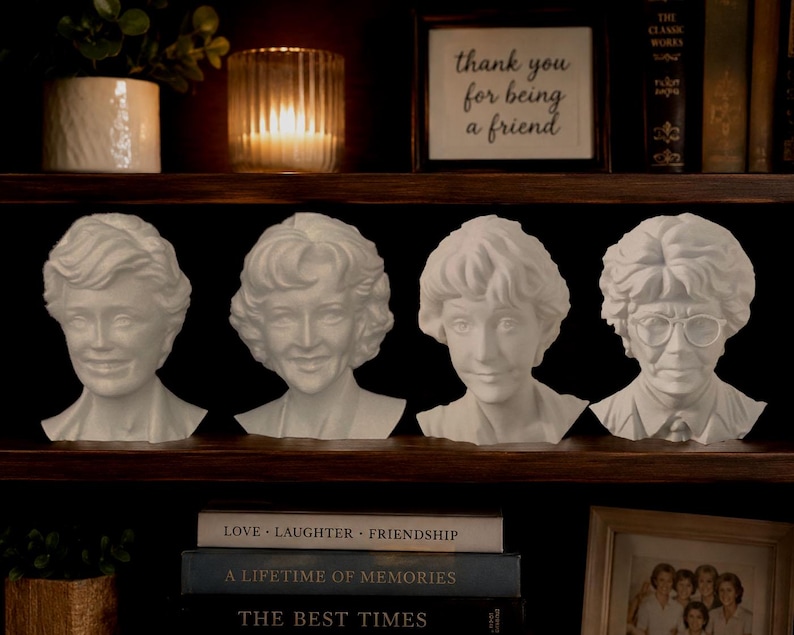 May include: Four white busts of women with different hairstyles and expressions are displayed on a dark wooden shelf. The busts are arranged in a row. A framed sign above reads "thank you for being a friend."