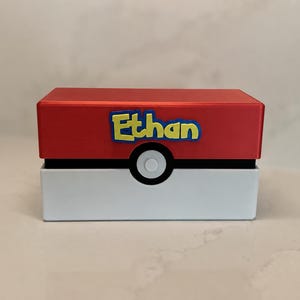 May include: A rectangular storage box designed to resemble a red and white ball. The top half is red and the bottom half is white, separated by a black band with a central white circle. The name Ethan is displayed in yellow letters with a blue outline.