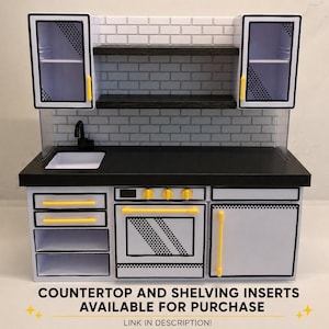 May include: A miniature kitchen playset featuring a white and black comic-book style design with yellow handles. The unit includes a black countertop, a sink with a black faucet, an oven, cabinets, and two open shelves against a white brick backsplash.