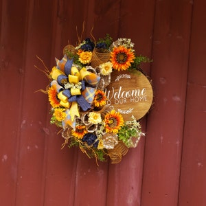 Puerta de entrada de otoño, corona de puerta de porche con girasoles y letrero de bienvenida manchado a nuestro hogar