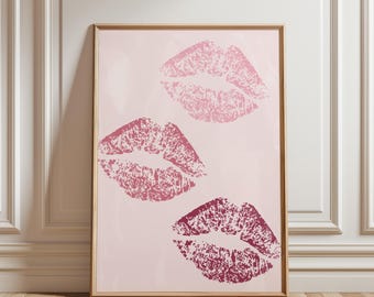 May include: A framed art print featuring three lip prints in shades of pink and burgundy on a light pink background. The artwork is displayed in a wooden frame, suitable for wall decor.