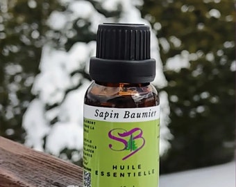 May include: A small amber glass bottle with a black cap, labelled "Sapin Baumier" in white text. The bottle contains essential oil and has a green label with a purple logo and the text "Huile Essentielle 18 ml".