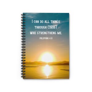 Könnte beinhalten: Spiralgebundenes Notizbuch mit einem Sonnenuntergang über Wasser auf dem Cover. Der Einband zeigt den weißen Text "I CAN DO ALL THINGS THROUGH CHRIST WHO STRENGTHENS ME. PHILIPPIANS 4:13" vor dem Hintergrund einer hellen Sonne und Wasser.