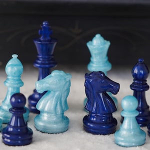 May include: A set of blue and light blue chess pieces. The pieces include a king, queen, knight, bishop, and pawn. The pieces are made of plastic and have a glossy finish.