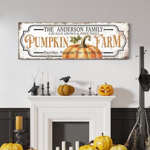 Può includere: Un cartello bianco con lettere nere che recita "The Anderson Family Locally Grown & Open Daily Pumpkin Farm Hayrides Pumpkin Pies Apple Cider". Il cartello ha un aspetto vintage e presenta una grande zucca arancione con foglie verdi.