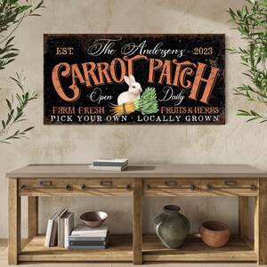 May include: A black and orange sign with the text "The Anderson's Carrot Patch" and the dates "EST 2023". The sign also says "Open Daily", "Farm Fresh", "Pick Your Own", "Locally Grown", and "Fruits & Herbs". A white rabbit with a carrot in its mouth is pictured on the sign.