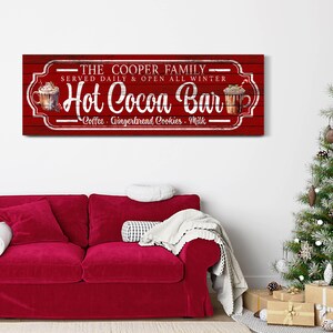 May include: Red wooden sign with white text that reads "THE COOPER FAMILY - SERVED DAILY & OPEN ALL WINTER - Hot Cocoa Bar - Coffee. Gingerbread Cookies. Milk". The sign has a vintage look and features a drawing of a mug of hot cocoa with whipped cream and a candy cane.