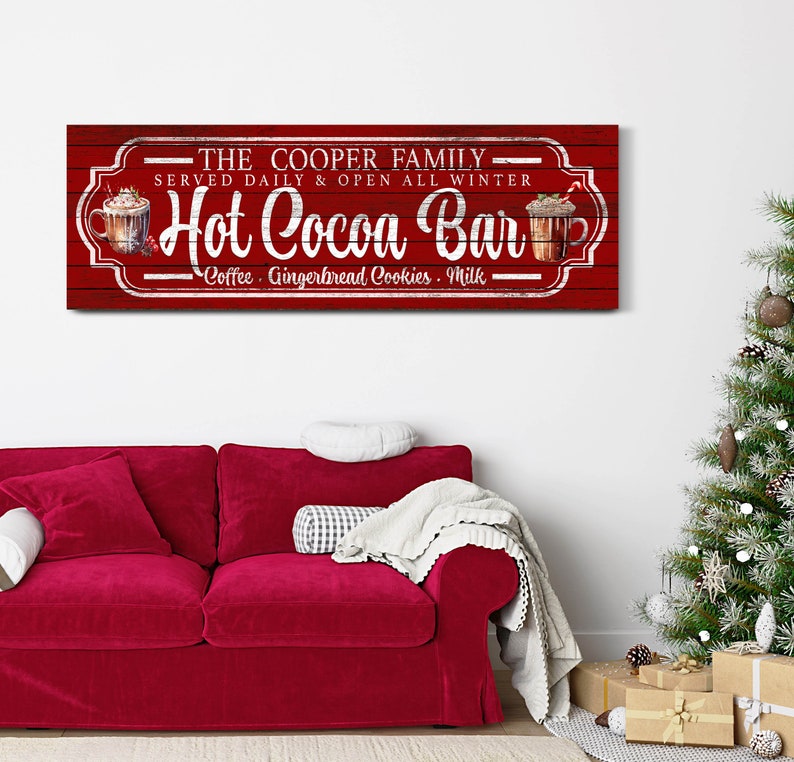 May include: Red wooden sign with white text that reads "THE COOPER FAMILY - SERVED DAILY & OPEN ALL WINTER - Hot Cocoa Bar - Coffee. Gingerbread Cookies. Milk". The sign has a vintage look and features a drawing of a mug of hot cocoa with whipped cream and a candy cane.
